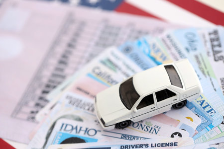 Toy car on big amount of driving licenses from different USA states on flag close up. Stack of driving license specimen cardsの写真素材