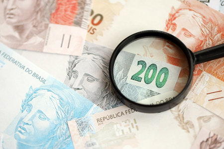 Brazilian reais banknotes and magnifying glass. The current Brazil real money bills and loupe lies on table in big amount. The concept of financial monitoring and taxation in Brazilの写真素材