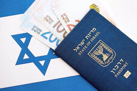Israel New Shekels banknotes and passport on flag. The current Israel money bills and biometrical pass lies on flag in big amount. The concept of travel and vacation in Israelの写真素材