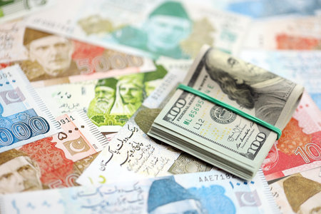 Bunch of US dollar bills lies on big amount of Pakistan rupees banknotes close up. American money...