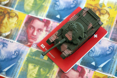 Swiss franc banknotes and toy tank on passport. The current francs money bills and tank lies on passport. The concept of army funds and weapons sales in Switzerlandの写真素材