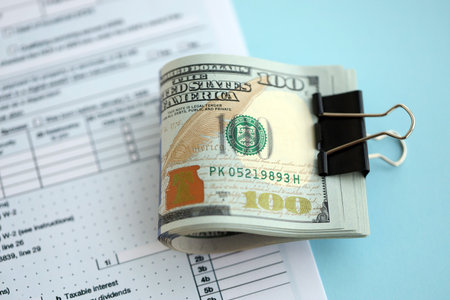 Big amount of United States dollar bills on table with 1040 individual income tax return form. Concept of taxation and accounting in United Statesの写真素材
