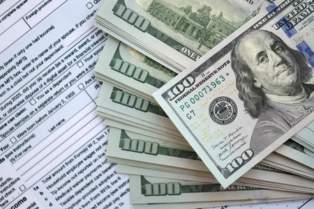 Big amount of United States USD dollar bills banknotes on table with 1040 individual income tax...