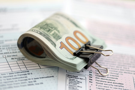 Big amount of United States hundred dollar bills in bunch on table with individual income tax return form close up. Concept of taxation and accounting in United Statesの写真素材