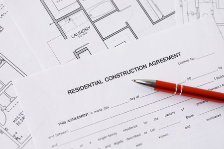 Pen on residential construction agreement and planning blueprints of residential building project...