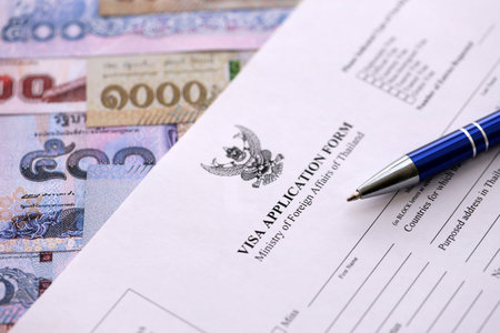 Visa application form to enter Thailand on table with pen and thai money bills close up
