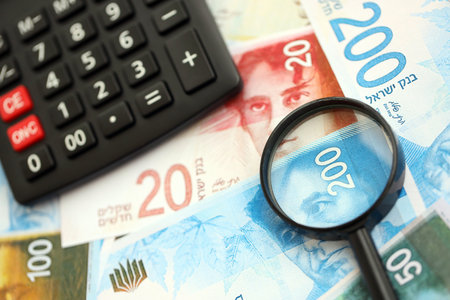 Israel New Shekels banknotes and calculator with magnifying glass. The current Israel money bills and calc with loupe lies on table in big amount. The concept of taxation and money count in Israelの写真素材