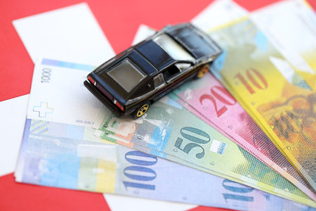 Swiss franc banknotes and toy car on flag. The current francs money bills and black car lies on flag. The concept of car ownership in Switzerlandの写真素材