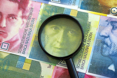 Swiss franc banknotes and magnifying glass. The francs money bills with loupe lies on table in big amount. The concept of financial monitoring and taxation in Switzerlandの写真素材