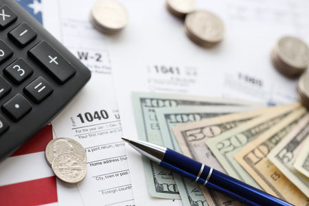 American US dollars money bills and coins with pen and calculator on IRS tax form blanks close up. Accounting and taxpaying period conceptの写真素材