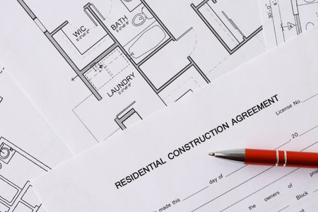 Pen on residential construction agreement and planning blueprints of residential building project...