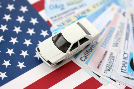 Toy car on big amount of driving licenses from different USA states on flag close up. Stack of driving license specimen cardsの写真素材