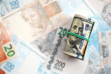 Roll of US dollar bills lies on big amount of Brazilian reais banknotes close up. American money roll lies on Brazil money bills. The concept of economics and currency exchange in Brazilの写真素材