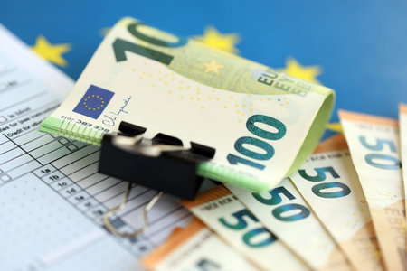 European euro currency money notes bunch on tax form and European union blue flag close up. Concept...