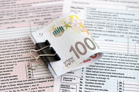 Israel New Shekels banknotes on tax form blank. The current Israel money bills lies on tax report document. The concept of taxation and taxpaying in Israelの写真素材