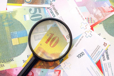 Swiss franc banknotes and magnifying glass. The current francs money bills with loupe lies on table...