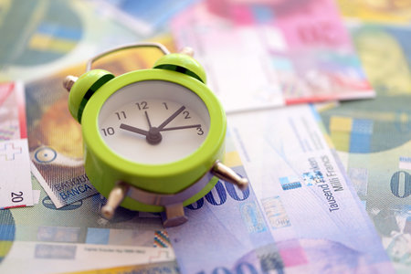 Swiss franc banknotes and alarm clock. The current francs money bills and clock lies on table in big amount. The concept of time management and income in Switzerlandの写真素材