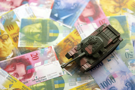 Swiss franc banknotes and toy tank. The current francs money bills and tank lies on table in big amount. The concept of army funds and weapons sales in Switzerlandの写真素材