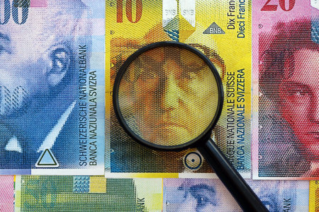 Swiss franc banknotes and magnifying glass. The money bills with loupe lies on table in big amount. The concept of financial monitoring and taxation in Switzerlandの写真素材