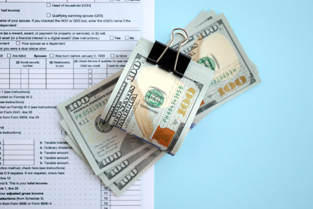 Big amount of United States hundred dollar bills on table with individual income tax return form close up. Concept of taxation and accounting in United Statesの写真素材