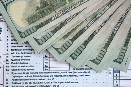 Big amount of United States dollar bills on table with 1040 individual income tax return form. Concept of taxation and accounting in United Statesの写真素材