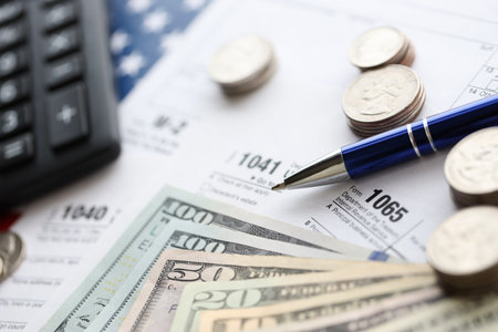 American US dollars money bills and coins with pen and calculator on IRS tax form blanks close up. Accounting and taxpaying period conceptの写真素材