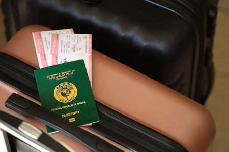 Federal Republic of Nigeria passport with tickets lies on touristic suitcase close up in airport waiting hall. Travel worldwide and international tourism conceptの写真素材