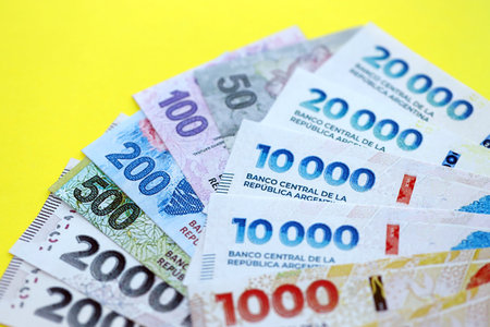 Argentine pesos money bills in big amount lies on yellow color table close up. Finance and banking...