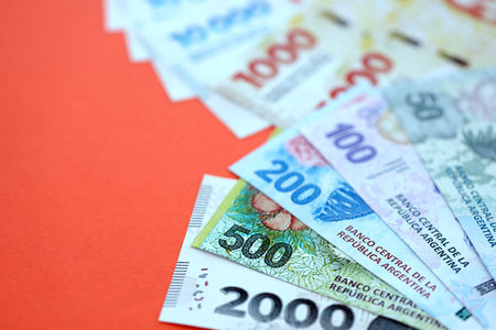 Argentine pesos money bills in big amount lies on red color table close up. Finance and banking conceptの写真素材