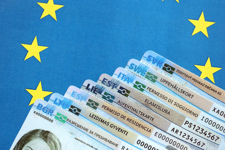 Permanent resident or residence permit cards lies on European Union flag. Paper specimen cards close...