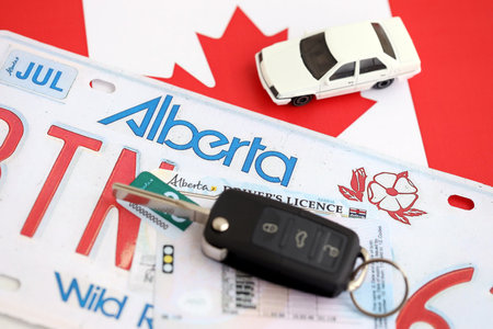 Alberta canadian car license plate and ignition key on flag of Canada close up. Driving permit and registration conceptの写真素材
