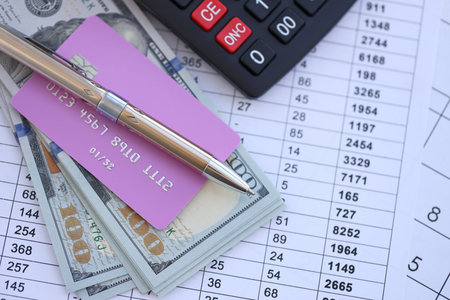 Credit card and pen with US dollar currency money bills banknotes on calculations document background. Business, financial operations and accounting in United States of Americaの写真素材