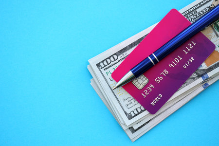 Credit card and pen with US dollar currency money bills banknotes on light blue background. Business, financial operations and accounting in United States of Americaの写真素材