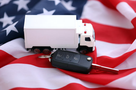 Ignition keys with remote control buttons and toy truck on United States flag. Concept of car driving in USA. Vehicle ownershipの写真素材