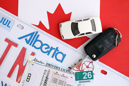 Alberta canadian car license plate and ignition key on flag of Canada close up. Driving permit and registration conceptの写真素材