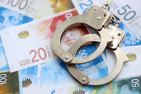 Israel New Shekels banknotes and handcuffs. The current Israel money bills and cuffs lies on table...