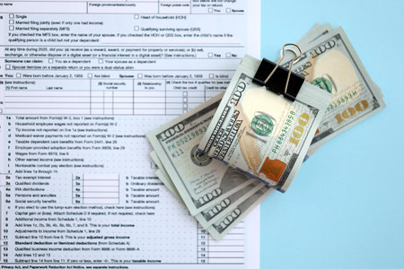 Big amount of United States hundred dollar bills on table with individual income tax return form...