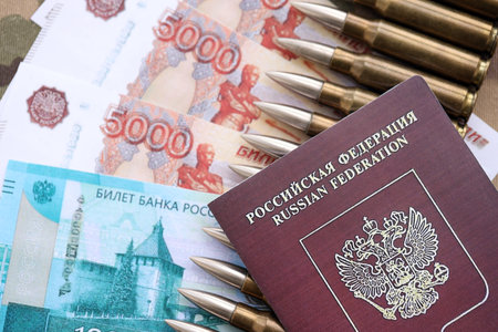 Money with bullets on passport and multicam camouflage fabric close up. Concept of army funds and invasion to Ukraineの写真素材
