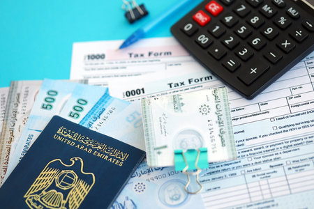 United Arab Emirates dirham money bills and calculator with tax form close up on blue. Taxation and...