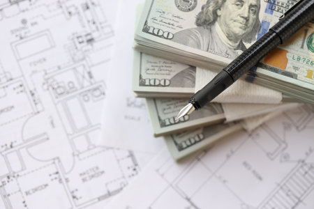 Big amount of US dollars money bills with pen and planning blueprints of residential building project close up. Investment and construction project conceptの写真素材