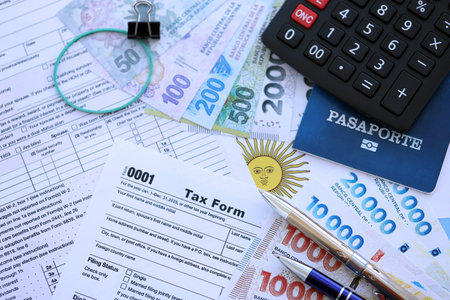 Argentine pesos money bills in big amount lies on table with pen, calculator, passport and tax forms close up. Finance and banking conceptの写真素材