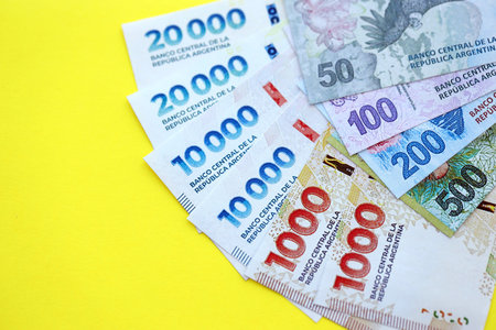 Argentine pesos money bills in big amount lies on yellow color table close up. Finance and banking...