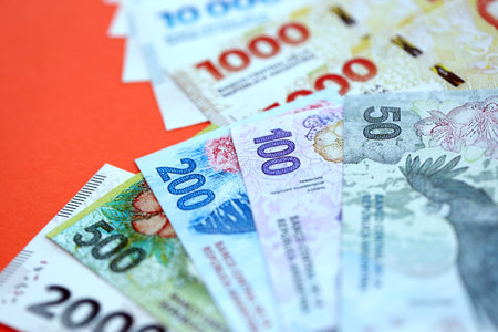 Argentine pesos money bills in big amount lies on red color table close up. Finance and banking...