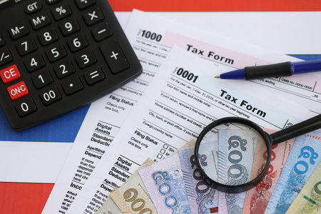 Thai baht money bills and calculator with tax form on flag close up. Taxation and accounting conceptの写真素材