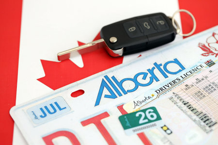 Alberta canadian car license plate and ignition key on flag of Canada close up. Driving permit and...