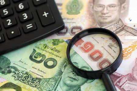 Thai baht currency money bills and calculator with magnifying glass close up. The concept of taxation and money countの写真素材