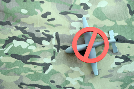 Unnamed grey toy drone model and red prohibition sign on camouflage fabric close up. Anti-aircraft warfare conceptの写真素材