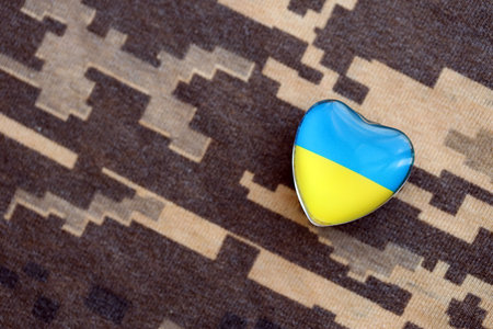 Glass heart with Ukrainian flag lies on military camouflage fabric. Concept of support and defend Ukraineの写真素材