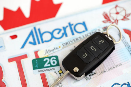 Alberta car license plate and ignition key on flag of Canada close up. Driving permit and registration conceptの写真素材