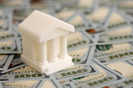 White toy bank on big amount of US dollar bills close up. Business and banking conceptの写真素材